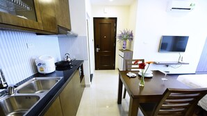 A compact kitchen with a double sink, a stove, and a dining area with a table and chairs. - Granda Legend Apartment (Hanoi)
