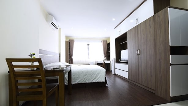 A hotel room with a bed, a desk, a chair, a wardrobe, and a TV. - Granda Legend Apartment (Hanoi)
