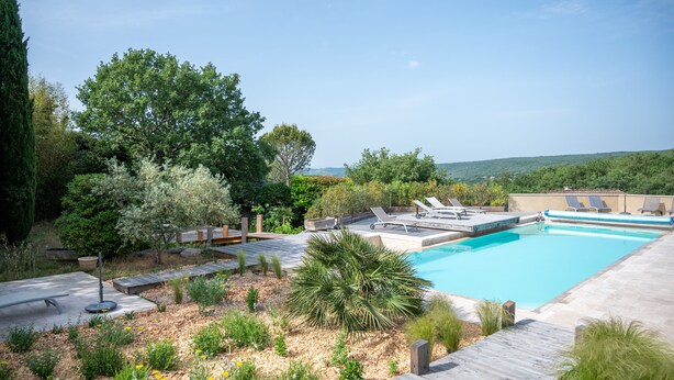 Une piscine avec une terrasse en bois, des chaises longues et une vue sur les collines.