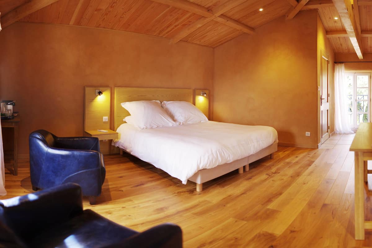 Een slaapkamer met een houten vloer, een bed met wit beddengoed, een blauwe stoel en een houten tafel.