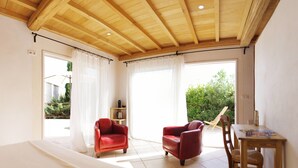 Une chambre avec un plafond en bois, un lit, une chaise rouge, une table en bois et une vue sur la verdure à l’extérieur.