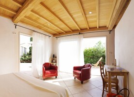 Un dormitorio con techo de madera, una cama, una silla roja, una mesa de madera y vistas a la vegetación exterior.