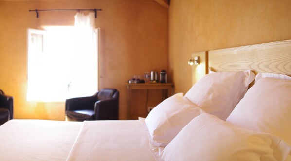 A hotel room with a bed, a chair, a small table with a coffee maker, and a window with curtains. - Les Carriers Maison D'hôtes (Vogue)