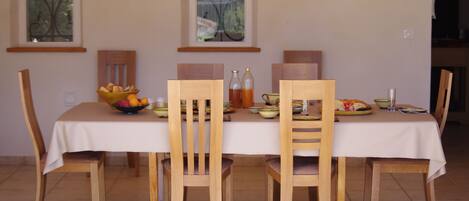Een eettafel met een witte tafelkleed, omringd door houten stoelen. Daarboven bevinden zich twee ramen, elk met een decoratieve lijst.