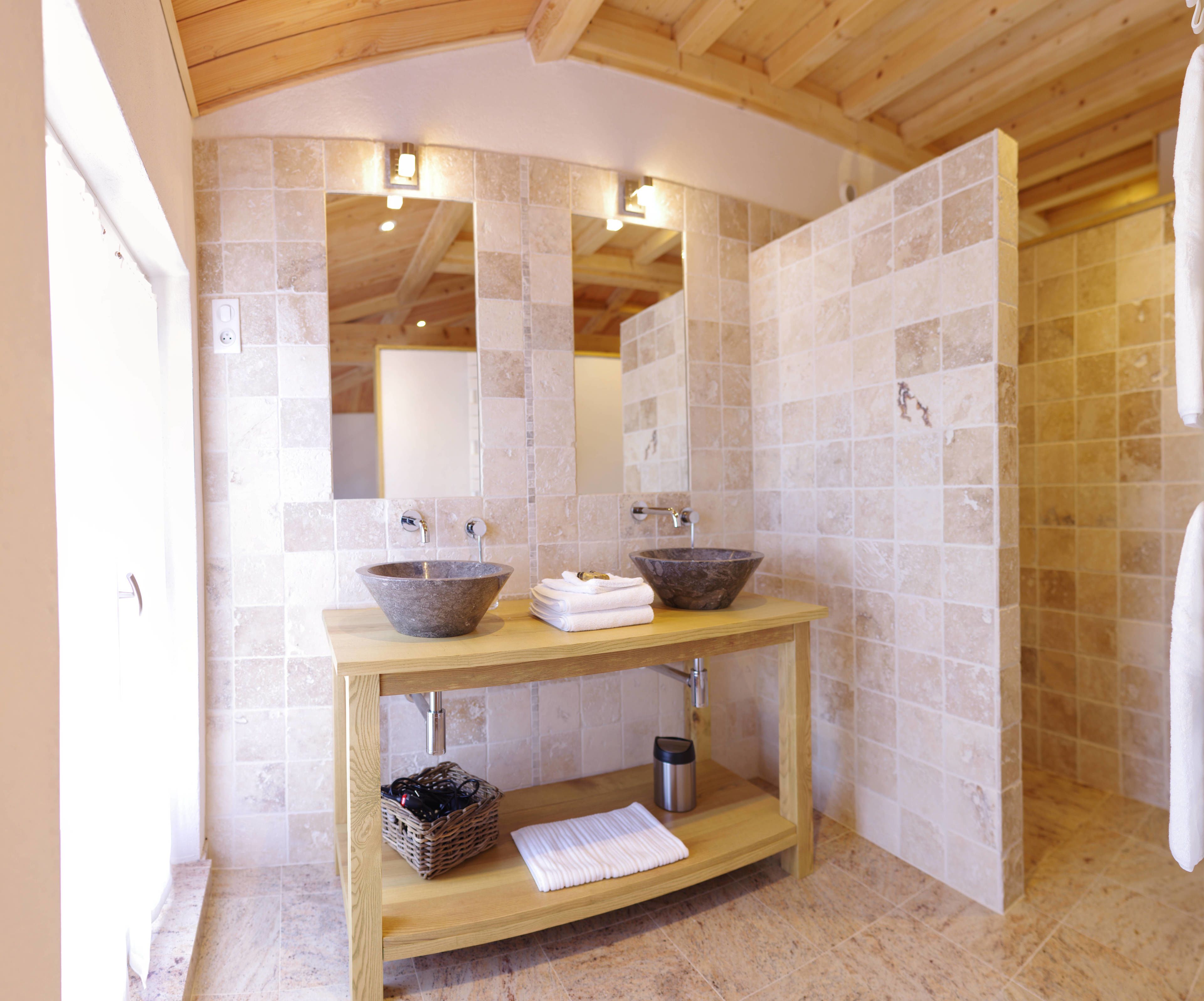 Un baño con dos lavamanos de piedra, un mueble de tocador de madera, un espejo y una pared con azulejos.