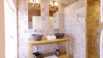 Un baño con dos lavamanos de piedra, un mueble de tocador de madera, un espejo y una pared con azulejos.