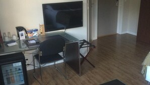 A living room with a flat-screen TV, a glass coffee table, a black sofa, and a small refrigerator. - Nordfjord Hotell - Bryggen (Stad)