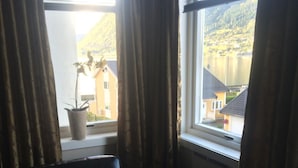 A room with a black leather chair, a potted plant, and a window with curtains. - Nordfjord Hotell - Bryggen (Stad)