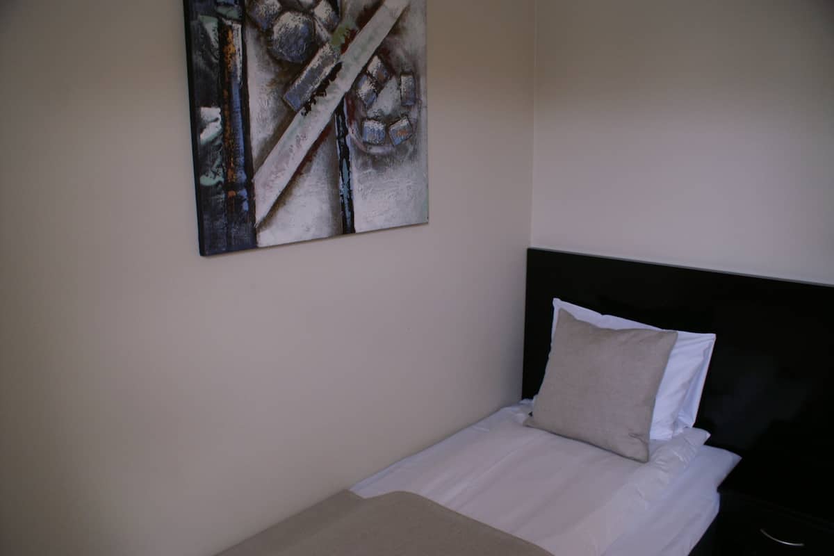 Uma cama bem arrumada com lençóis brancos e um travesseiro bege, uma cabeceira preta e uma obra de arte abstrata na parede.