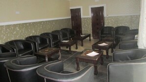 Un salón de conferencias con sillas de cuero negro y mesas de madera, dos puertas y un papel tapiz estampado.
