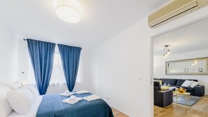 A modern bedroom with a bed, blue curtains, a large mirror, and a living area with a sofa and a table. - Superior Stay Zagreb (Zagreb)
