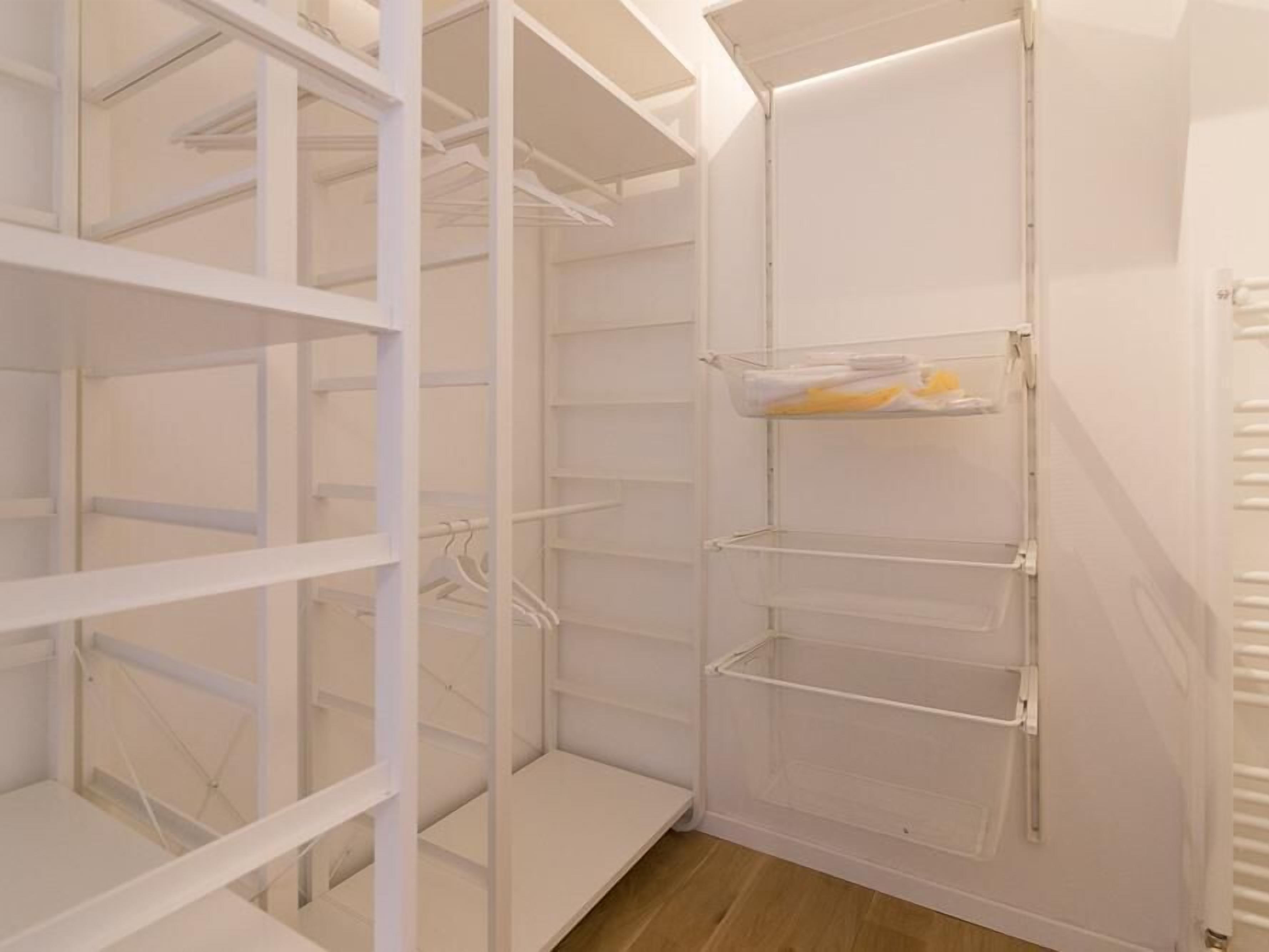 A white closet with multiple shelves and hanging space, featuring a clear plastic storage box on one of the shelves.