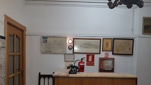 A reception desk with a wooden finish, a fire extinguisher, and several framed certificates or documents on the wall. - Pensión Martín (Jaén)