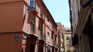 A narrow cobblestone street lined with buildings, including a red building with a blue sign reading "Pension" and another with a sign reading "Calle Chinchilla." - Pensión Martín (Jaén)