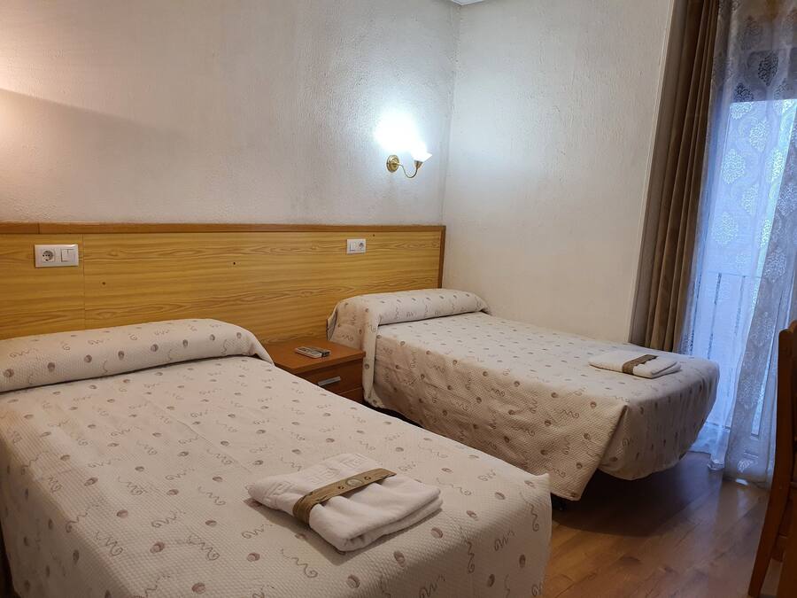 Ein Hotelzimmer mit zwei Einzelbetten, Holzkopfteilen, einem Nachttisch mit Fernbedienung und einer wandmontierten Lampe.