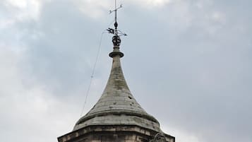 A historic stone tower with a clock, arched windows, and a weather vane.