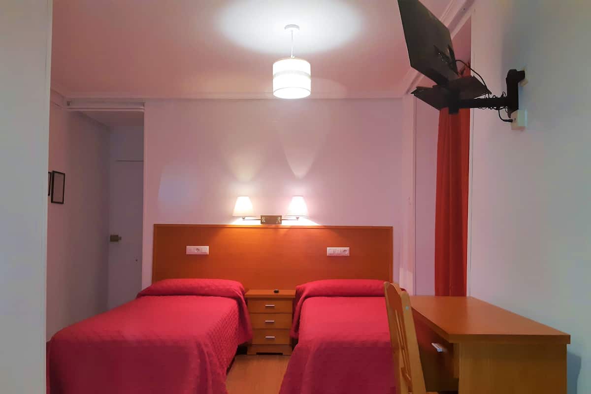 A room with two beds, a desk, and a ceiling lamp.