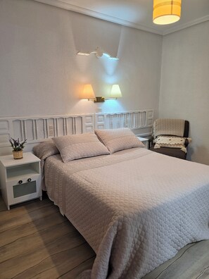 A bedroom with a white bed, a nightstand, a lamp, and a chair.