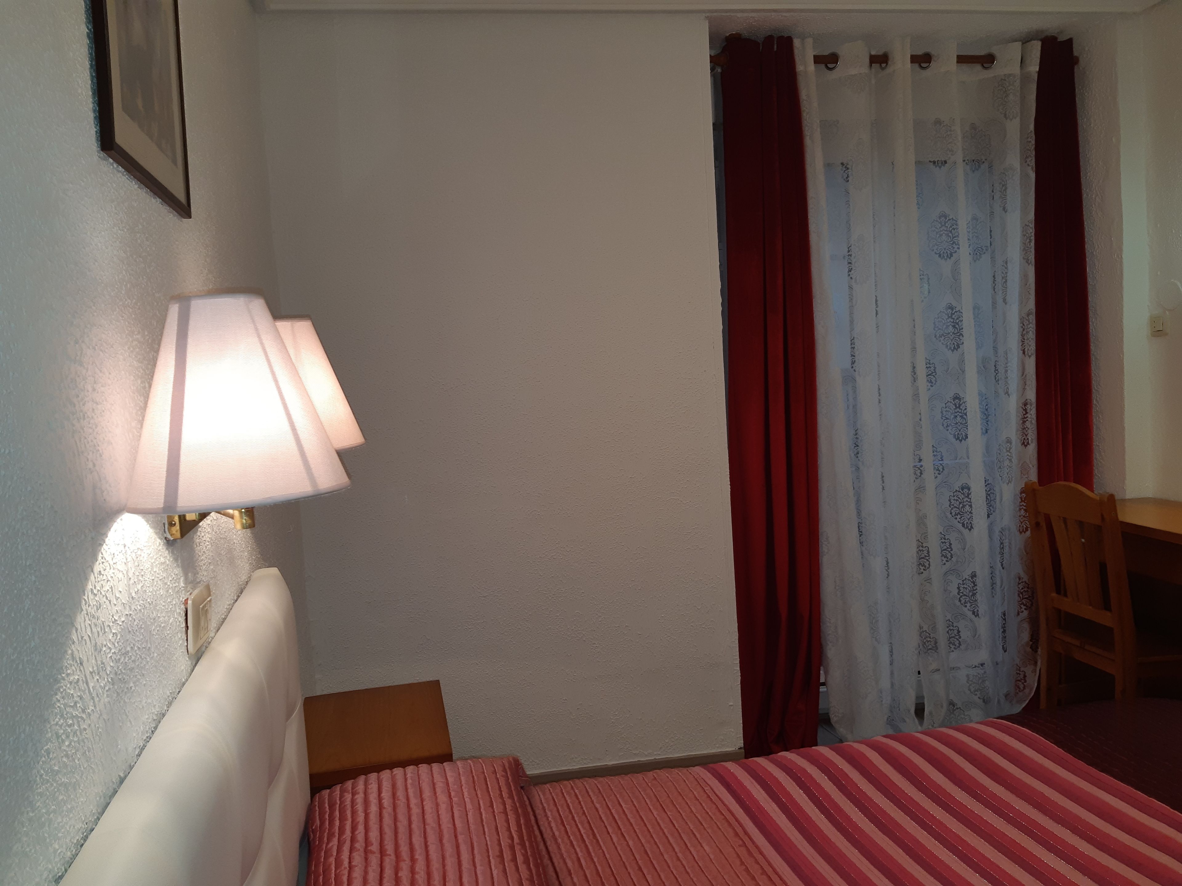 Habitación de hotel con cama, escritorio, silla, lámpara y ventana con cortinas.