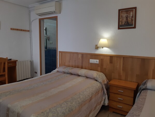 A bedroom with a bed, bedside tables, a desk, and an air conditioning unit.