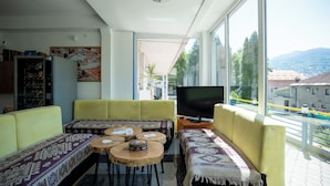 A living room with a sofa, a television, and a view of a cityscape through large windows.