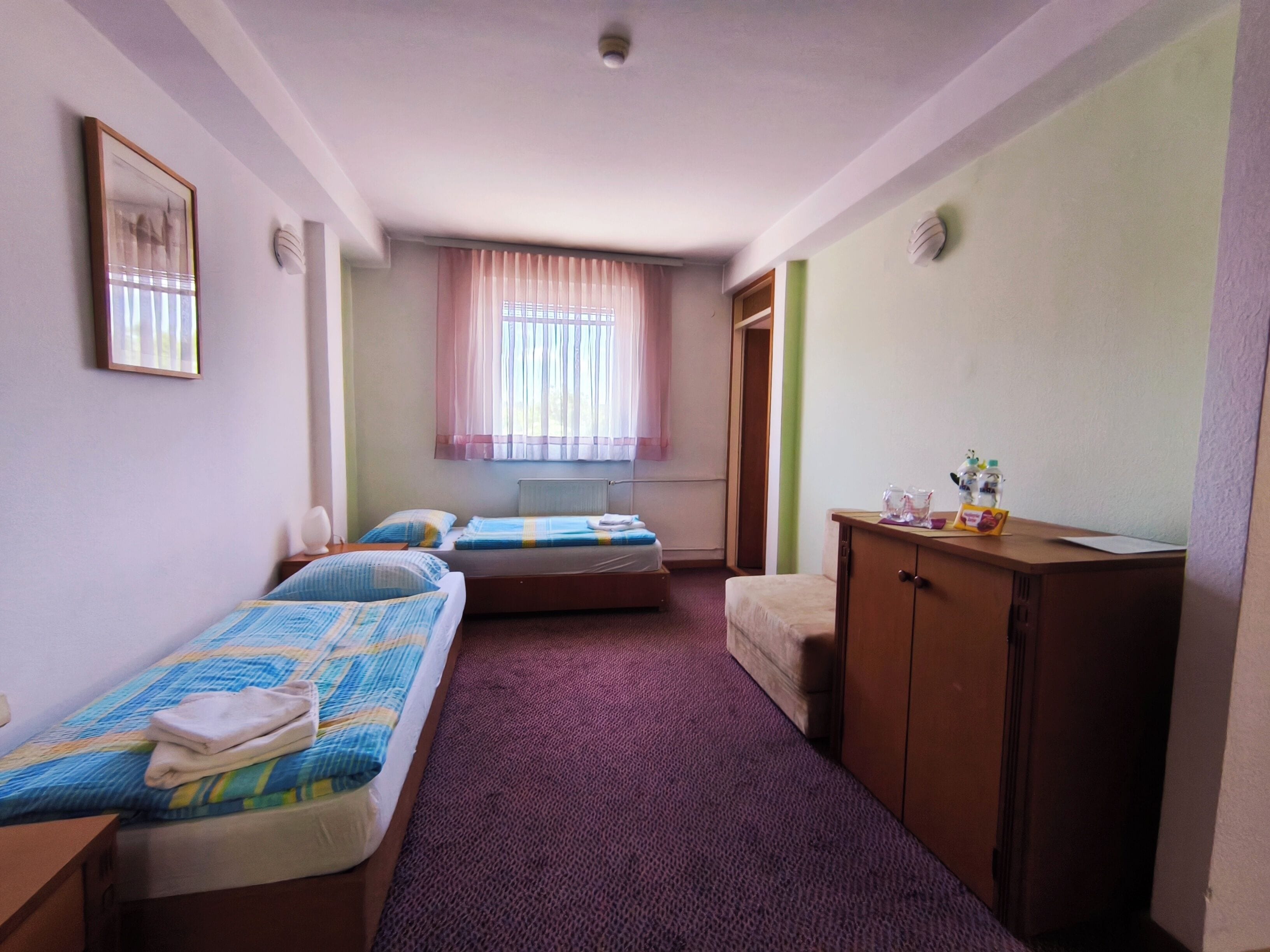 A room with two beds, a wooden cabinet, a radiator, and a window with curtains.