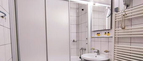 A bathroom with a shower, two sinks, a mirror, and a towel rack.