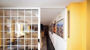 A hallway with a reception desk, framed pictures on the wall, and a sign indicating the direction to the restaurant.