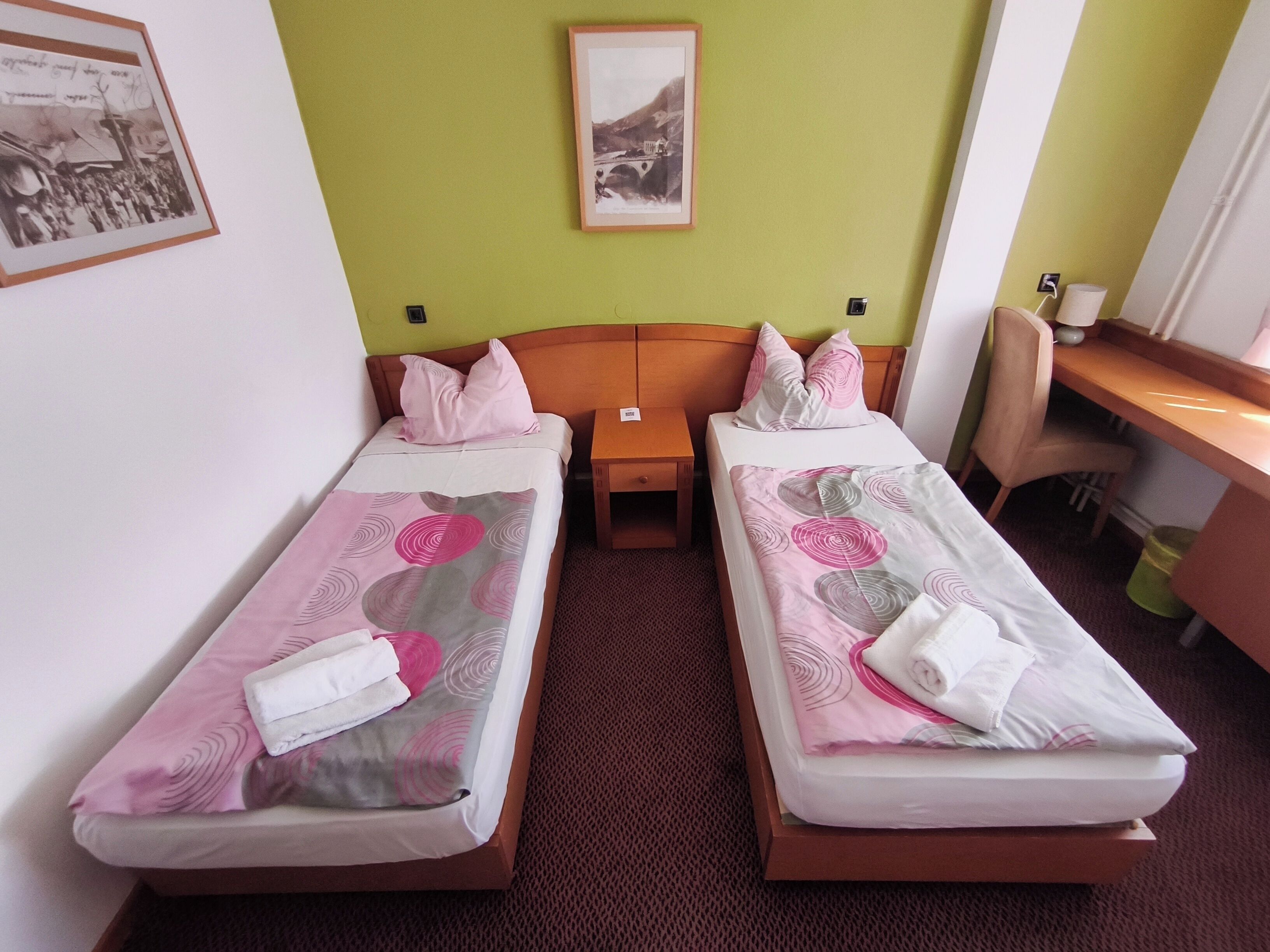 Habitación doble con dos camas, un escritorio, una silla, un cuadro en la pared y piso alfombrado.