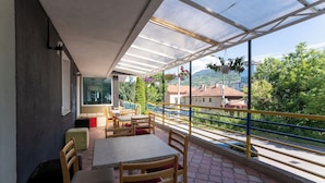 A covered outdoor seating area with tables and chairs, a view of the street, and a railing.