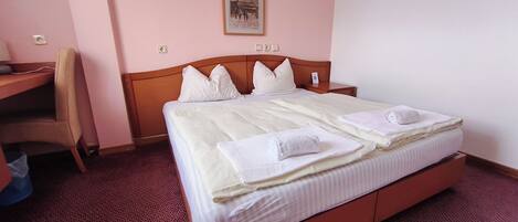 A hotel room with a bed, a desk, a chair, and a wall-mounted picture.