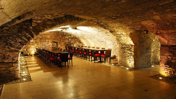 A stone-walled dining area with a long table and chairs, illuminated by overhead lighting. - Das Spritzenhaus (Eltville am Rhein)