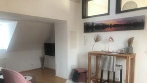 A modern living room with a pink chair, a wooden desk with two striped chairs, a flat-screen TV, and artwork on the wall. - Das Spritzenhaus (Eltville am Rhein)