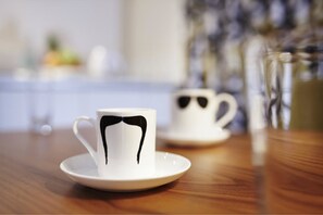 Dos tazas blancas con diseños de bigote negro sobre una mesa de madera.