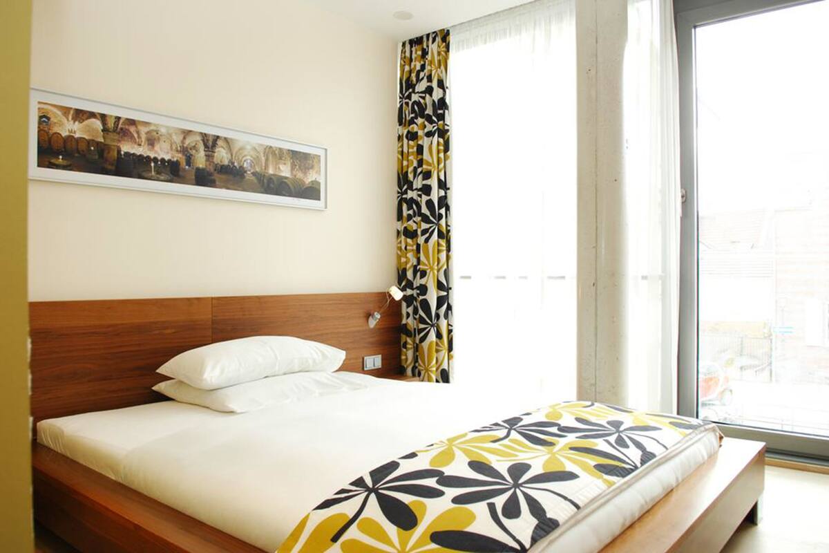 A hotel room with a bed, a painting on the wall, and a window with curtains.
