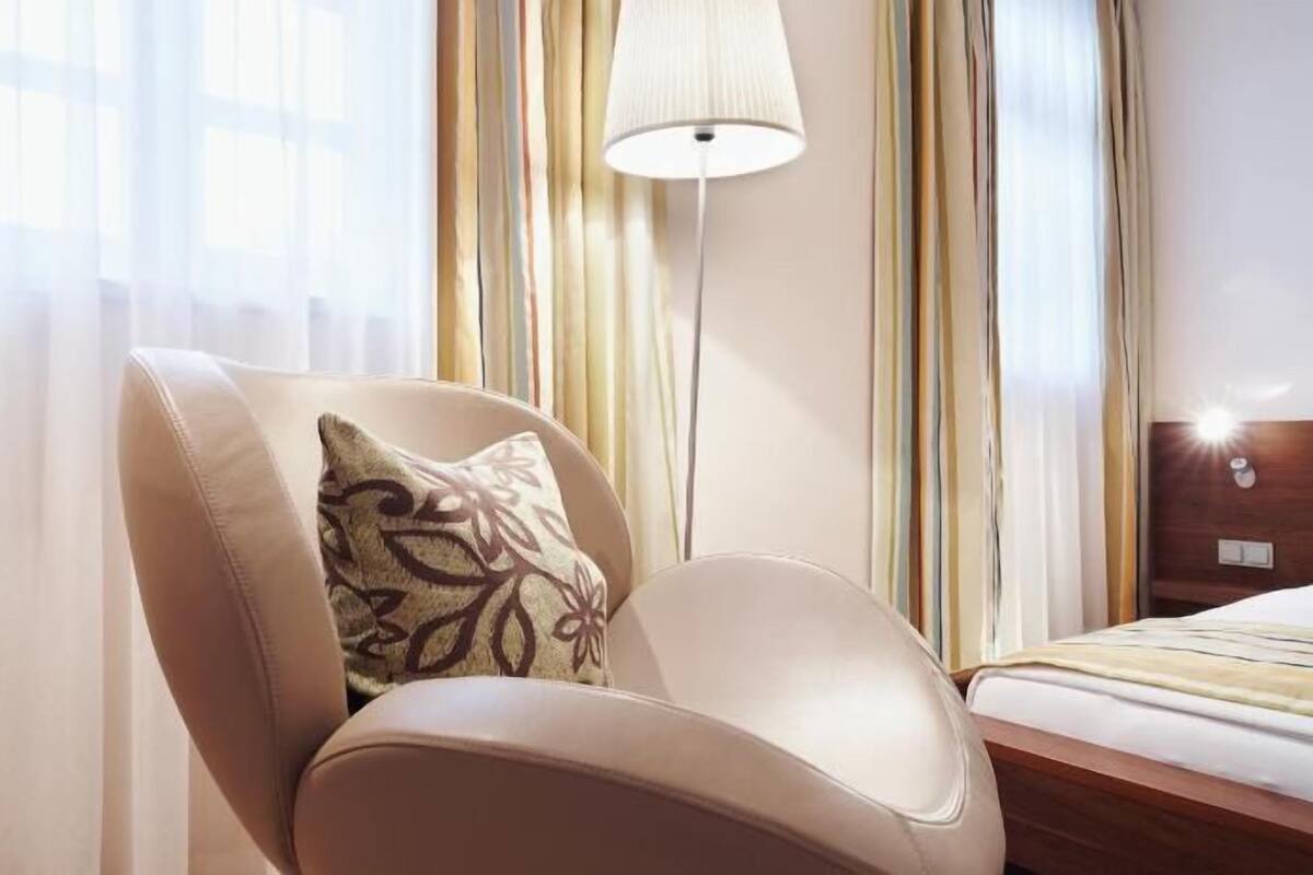 A hotel room with a leather armchair, a bedside table, a lamp, and curtains.