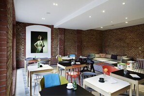 Un comedor moderno con paredes de ladrillo, un cuadro grande y una mezcla de sillas y mesas coloridas.