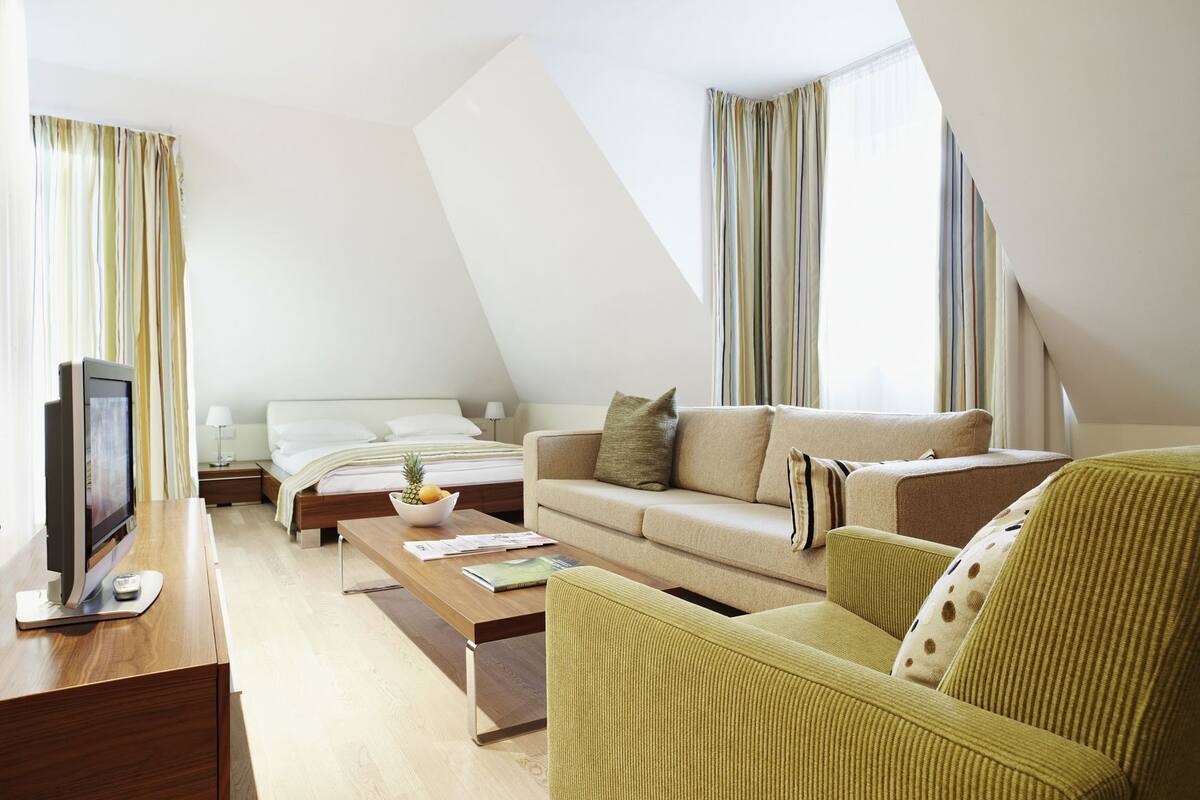 A modern hotel room with a bed, sofa, TV, and a dining table.