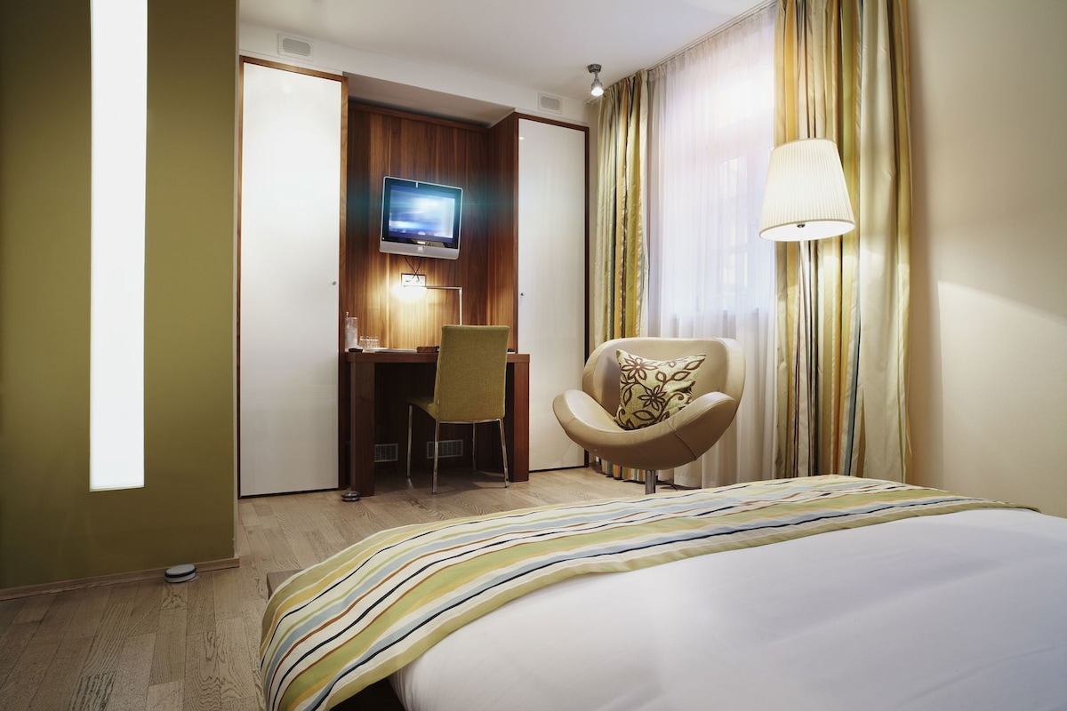 A hotel room with a bed, a desk with a computer, a chair, and a TV.