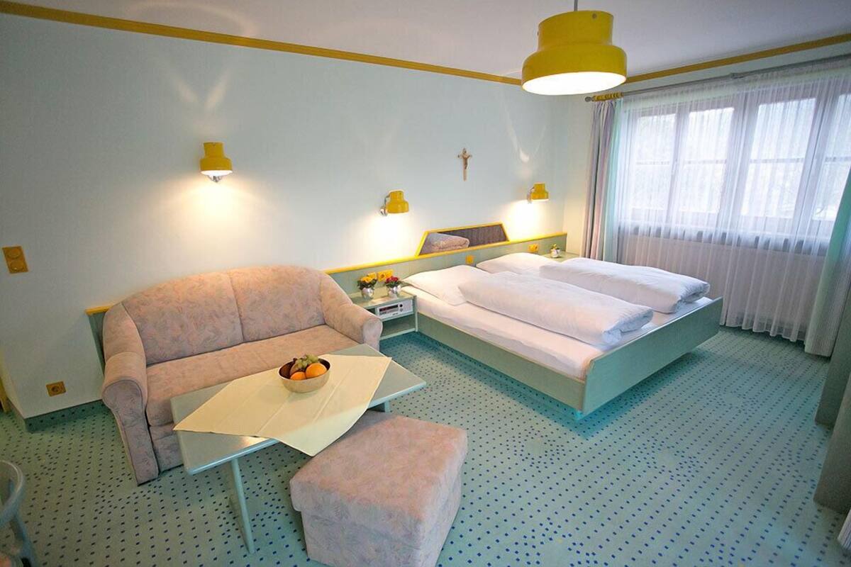 A hotel room with a bed, a sofa, a small table, and a nightstand.