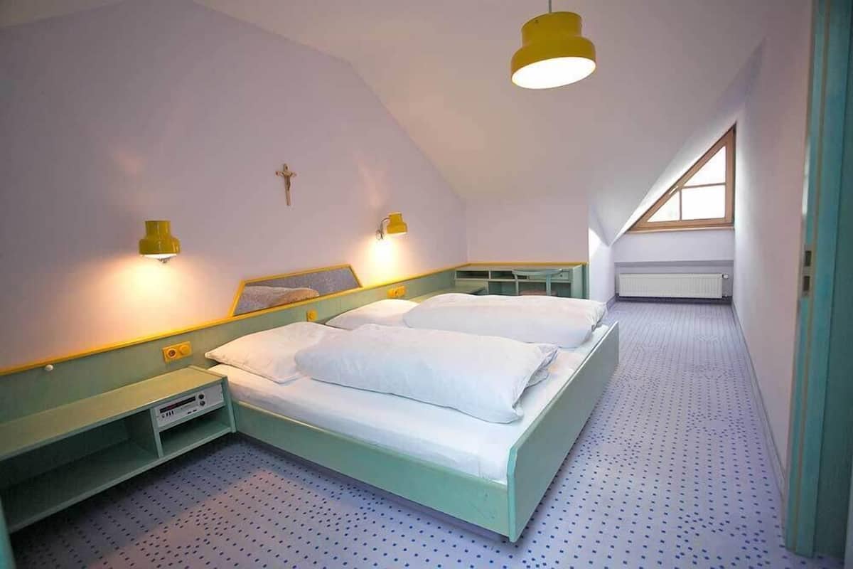 A bedroom with a bed, bedside tables, a wall-mounted light, and a window.