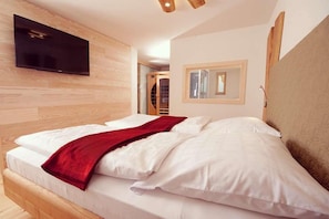A bedroom with a bed, a TV mounted on the wall, a mirror, and a wooden headboard. - Hotel-Gasthof zum Bach (Neukirchen Beim Heiligen Blut)