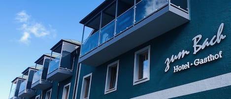A hotel named 'Zum Bach' with a modern design, featuring balconies and large windows.