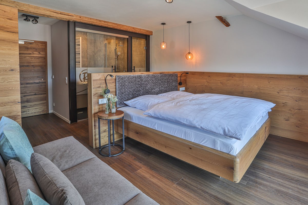 A bedroom with a wooden bed, a wooden headboard, a small round table with a lamp, and a sofa.