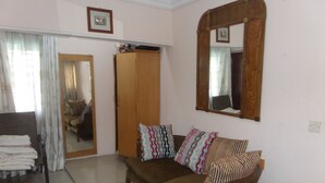 A living room with a brown sofa, patterned cushions, a wooden wardrobe, a mirror, and a framed picture on the wall. - House No 12B (Lagos)