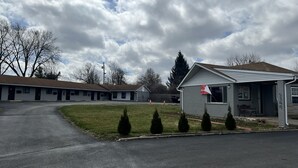 Motel amb diverses habitacions, un aparcament i una petita zona verda amb arbustos podats.