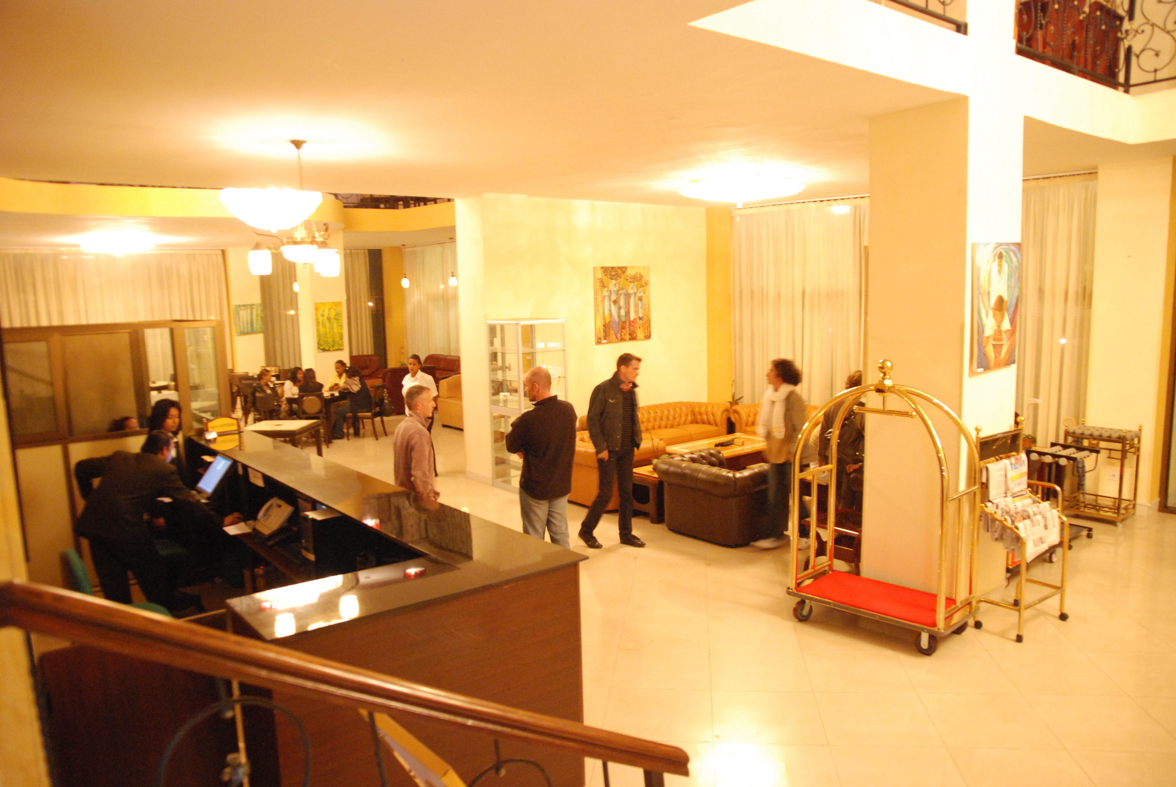 A hotel lobby with a reception desk, seating areas, and a luggage cart.