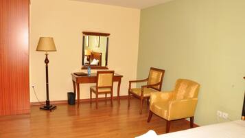 A hotel room with a wooden floor, a desk with a chair, a bed, a lamp, and a mirror.