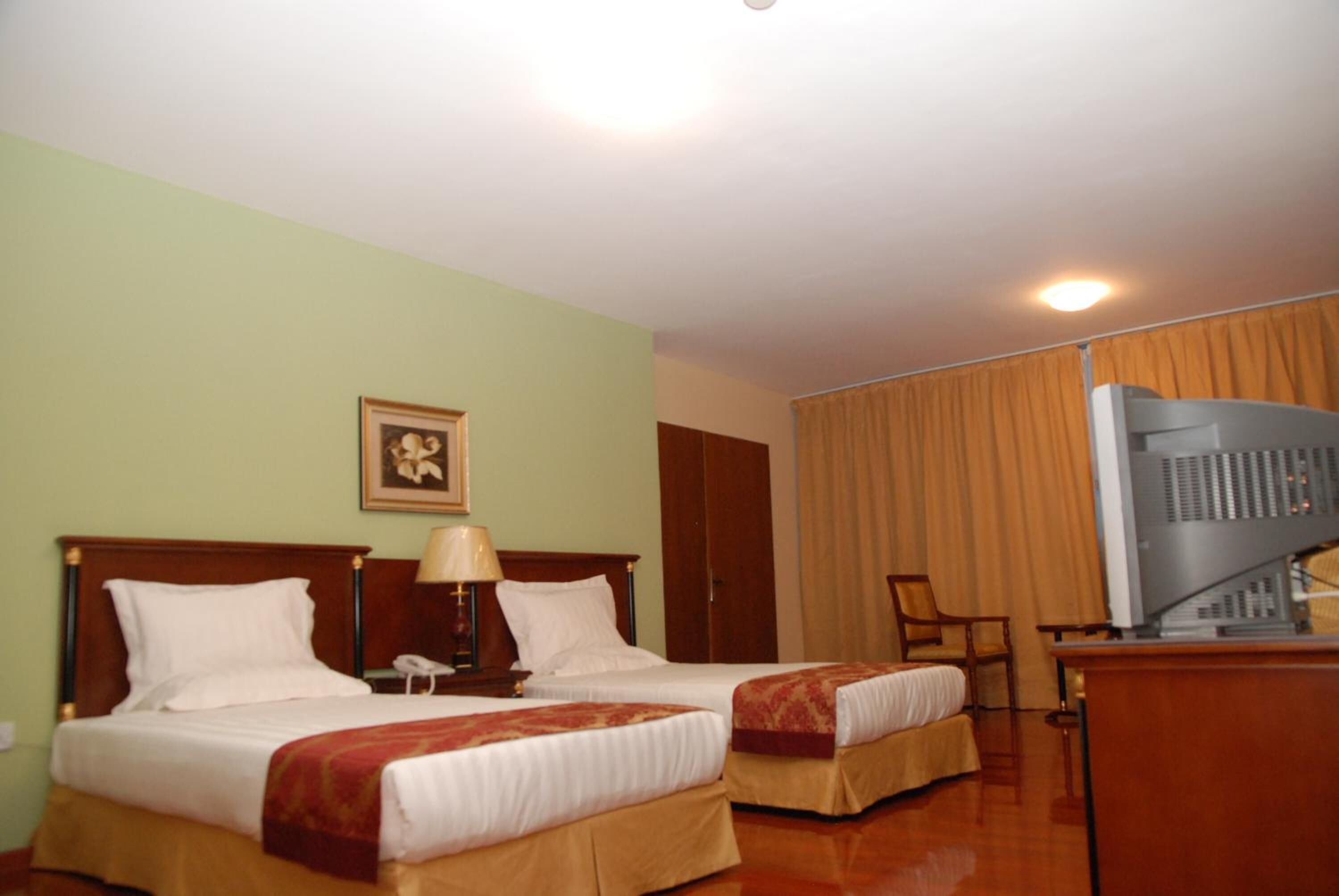 A hotel room with two beds, a desk with a television, and a framed picture on the wall.