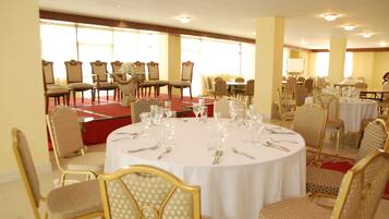 A banquet hall with round tables set for dining, surrounded by upholstered chairs.